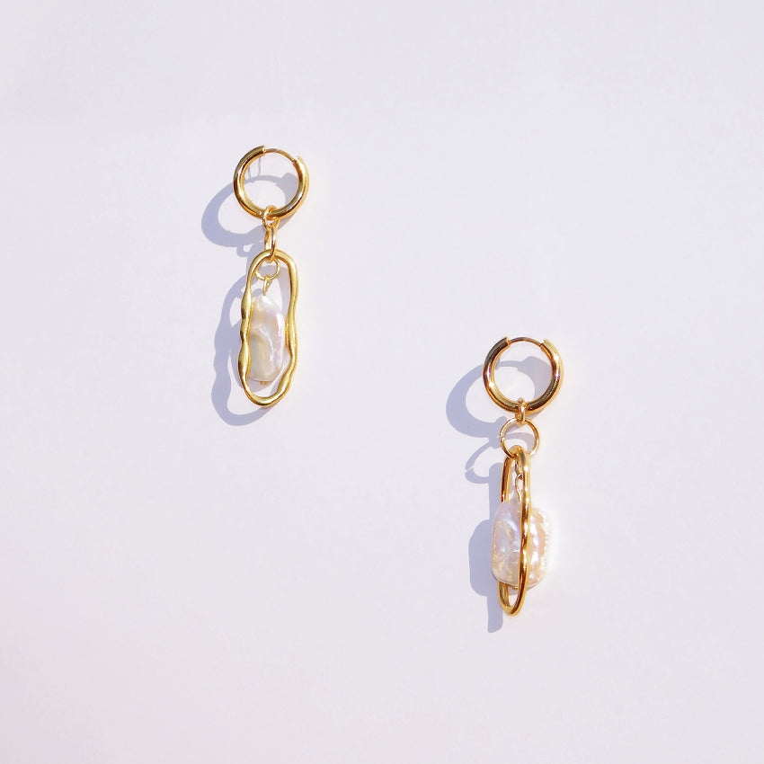 Pair of 18k gold plated stainless steel earrings with freshwater keshi pearls in the middle on a white background